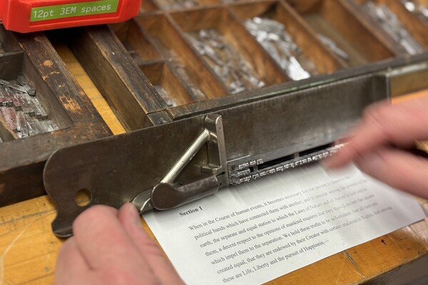A hand preparing letterpress off a small paper with text.
