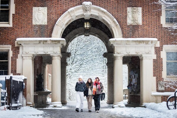 Three students walking under an arch in the snow on Penn’s campus.