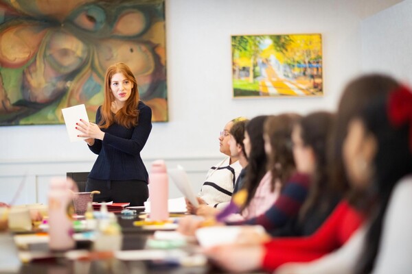 A professor standing at the head of a table talking to students.