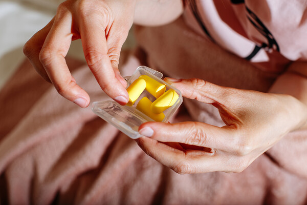 A person in bed taking earplugs out of a case.