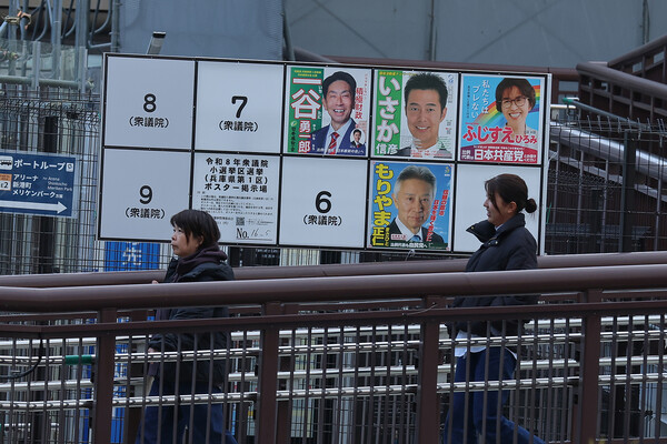 People walk in front of an election notice board displaying posters of candidates for the Lower House elections on the day of the election campaign kick-off on January 27, 2026 in Kobe, Japan.
