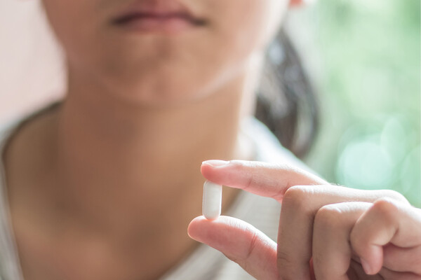 An adolescent holding a prescription pill.