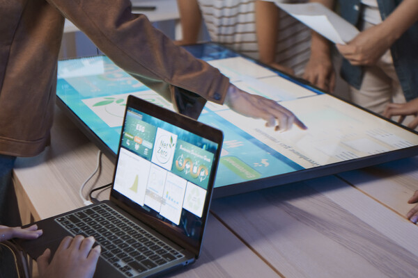 People working on a laptop and a screen looking at climate initiatives.