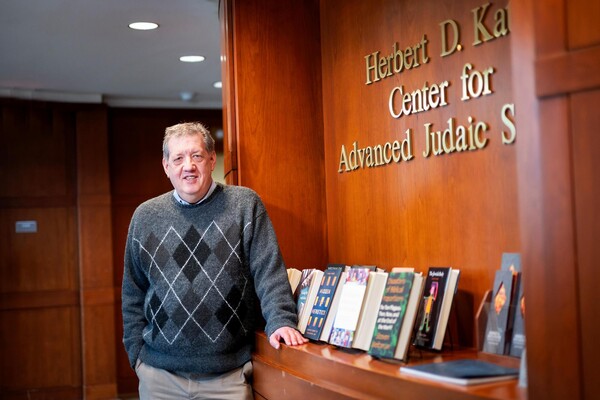 Steven Weitzman standing upright and smiling, facing forward, in the Library at the Herbert D. Katz Center for Advanced Judaic Studies, next to a wall with books on display