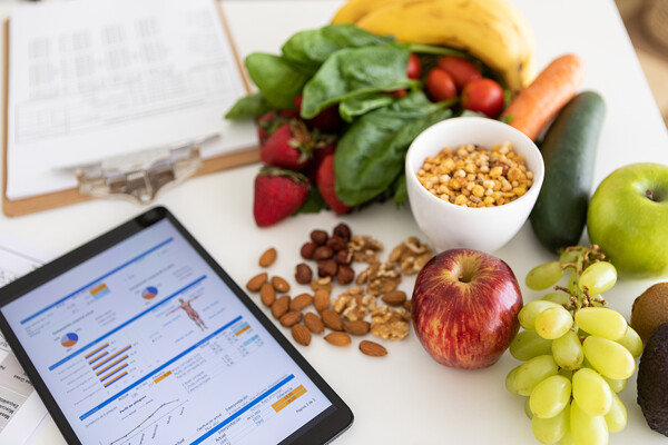 A tablet with biometric stats on a desk with fresh produce and legumes.
