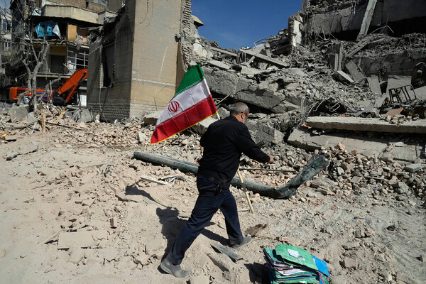 A person carries an Iranian flag to place on the site of an attack.