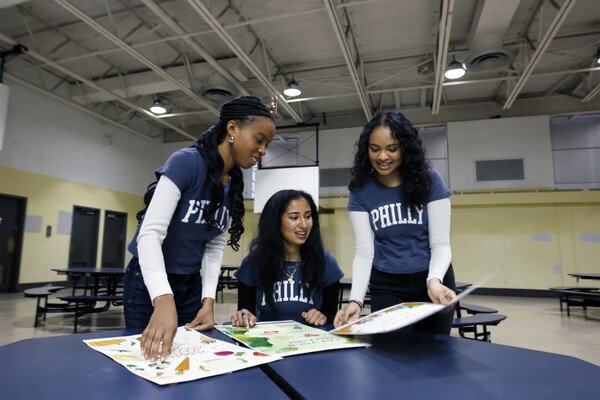 Three members of Nourish to Flourish working on computers in a school gymnasium.