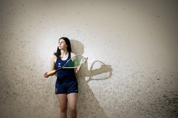 Jana Dweek holds a squash racket up against a wall with squash ball marks.