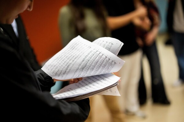 A student holding a composition sheet of music notes during while practicing their group performance.