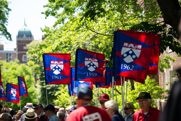 A procession of Penn alums alongside flags featuring the dates they graduated.