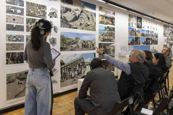 Ferda Kolatan (seated far right) in his studio pointing to photographs on the wall with onlookers.