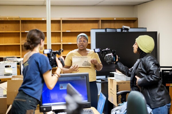 Two students take video of archivist holding up newspaper clipping.