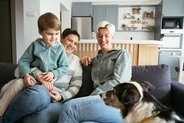 Two women sit on a couch with a child and dog.