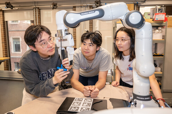 Three students working on a robotic arm in the GRASP lab