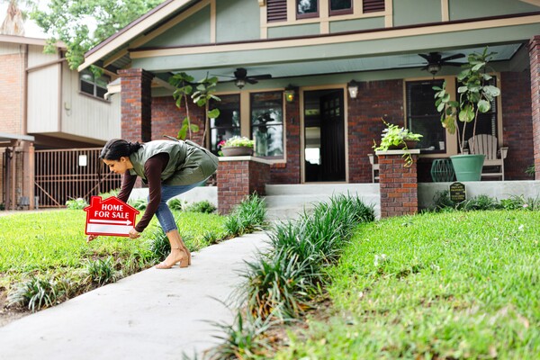 A person putting a Home for Sale sign in front of a home.