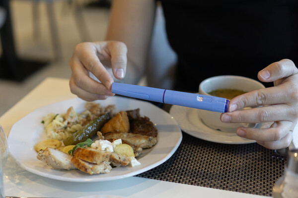 A person seated at a table holding a semaglutide pen over a plate of food.