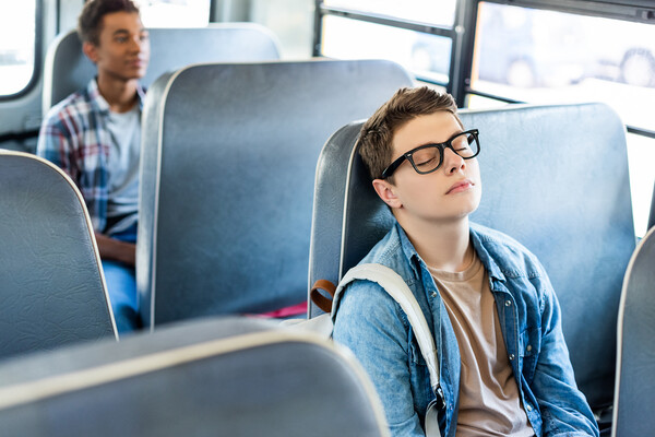 A high school student asleep on a school bus.